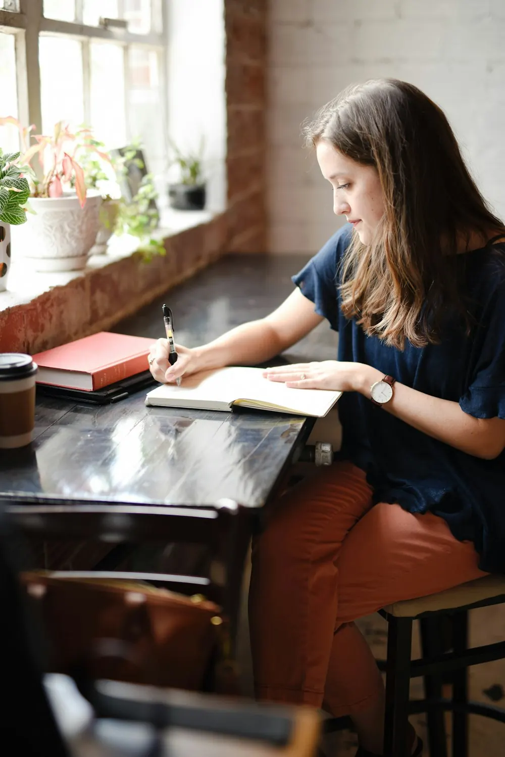 Student writing notes in a book by a window